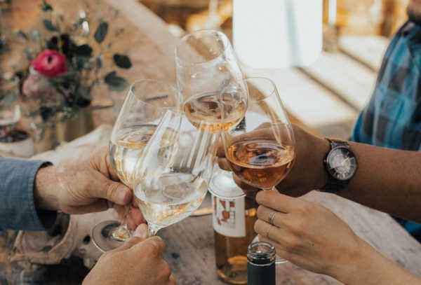 Four people toasting with glasses of wine around a table, enjoying a delightful gathering at a scenic vineyard in the Sierra Foothills.
