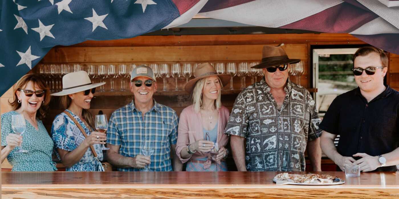 Group of six people gathered in front of a wine truck with an American flag banner.