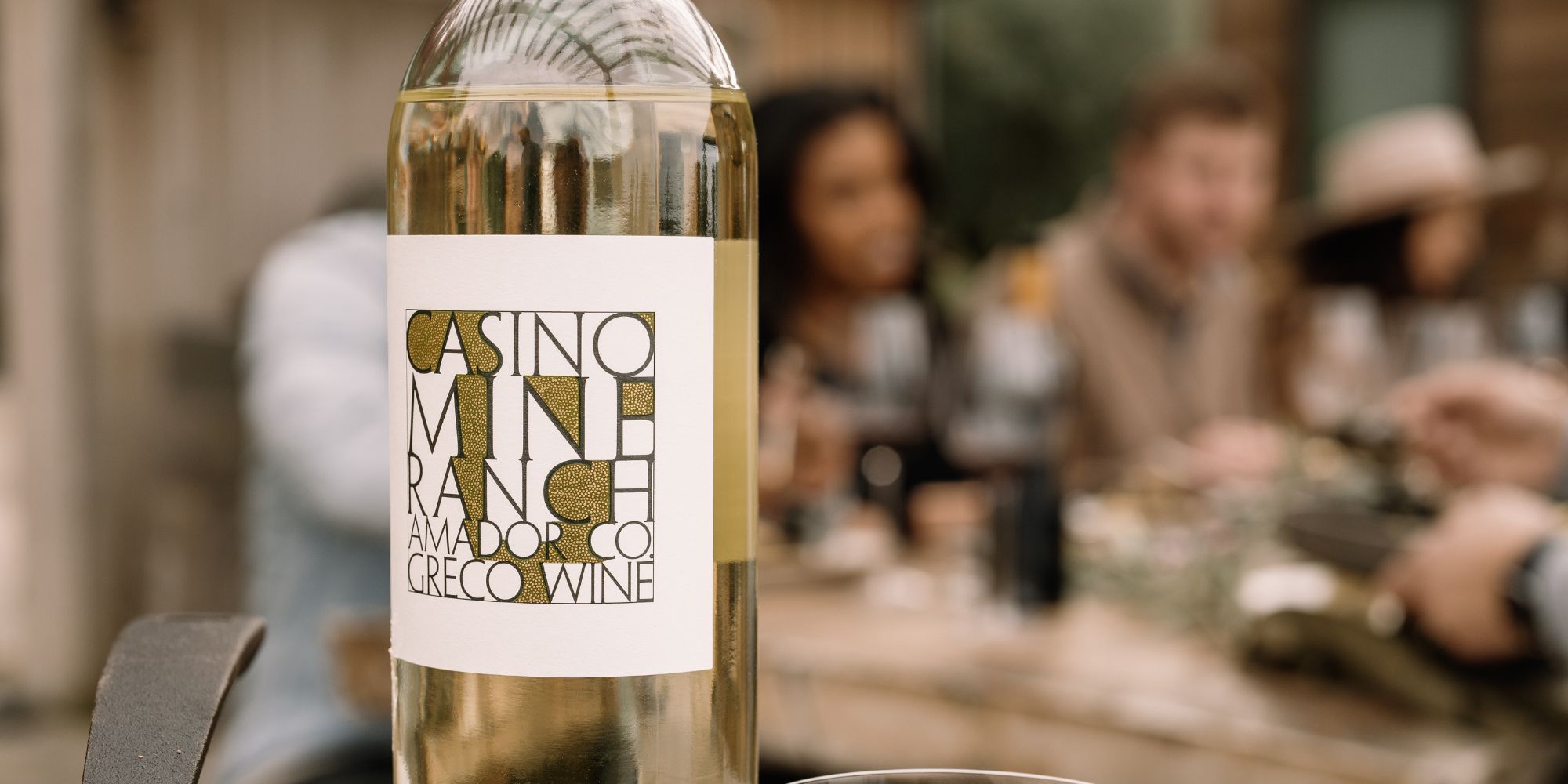 Casino Mine Ranch Greco wine bottle close up with a gathering of people blurred in the background.