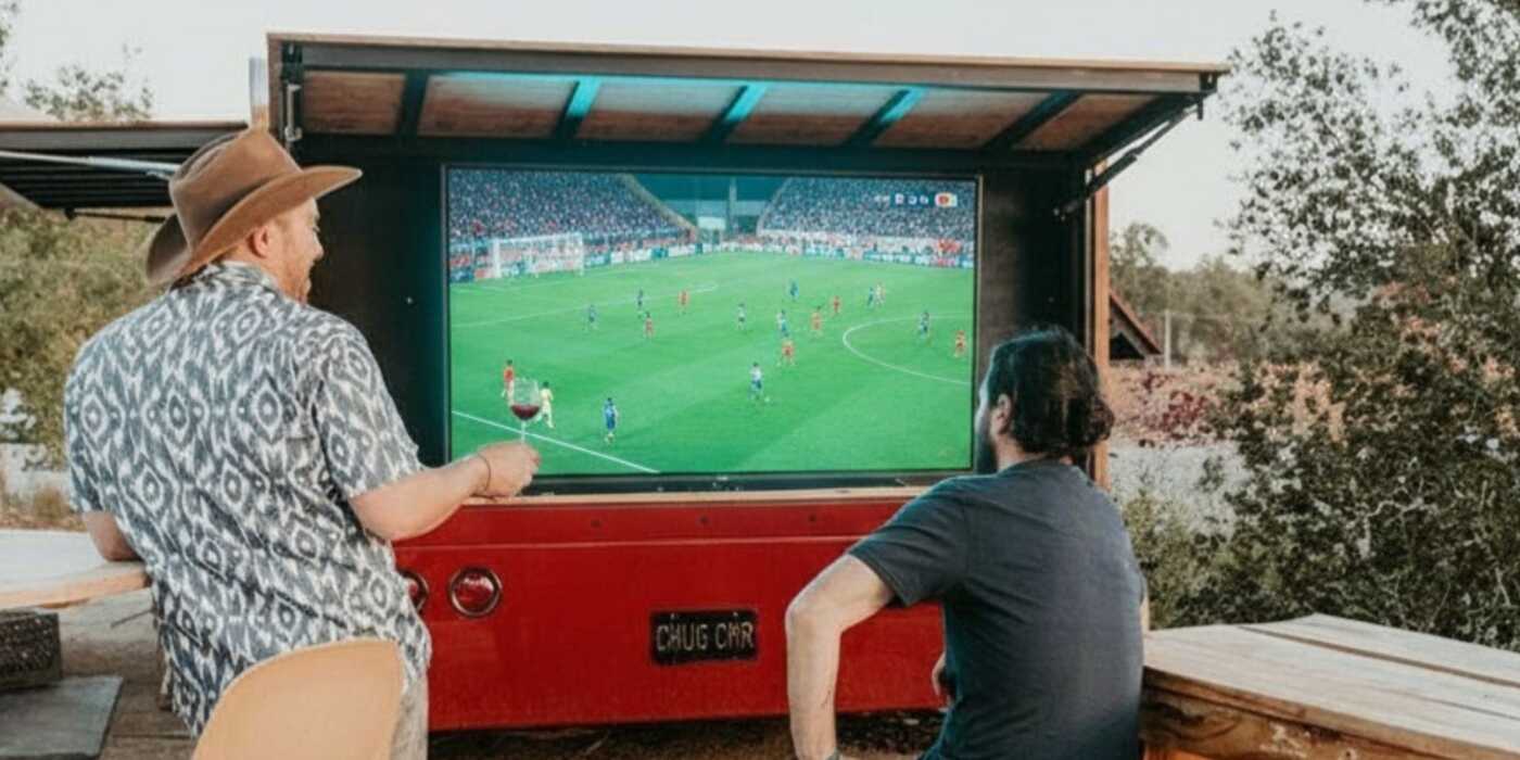 Two guys looking at a big screen at the Casino Mine Ranch Wine Truck watching the soccer matches.