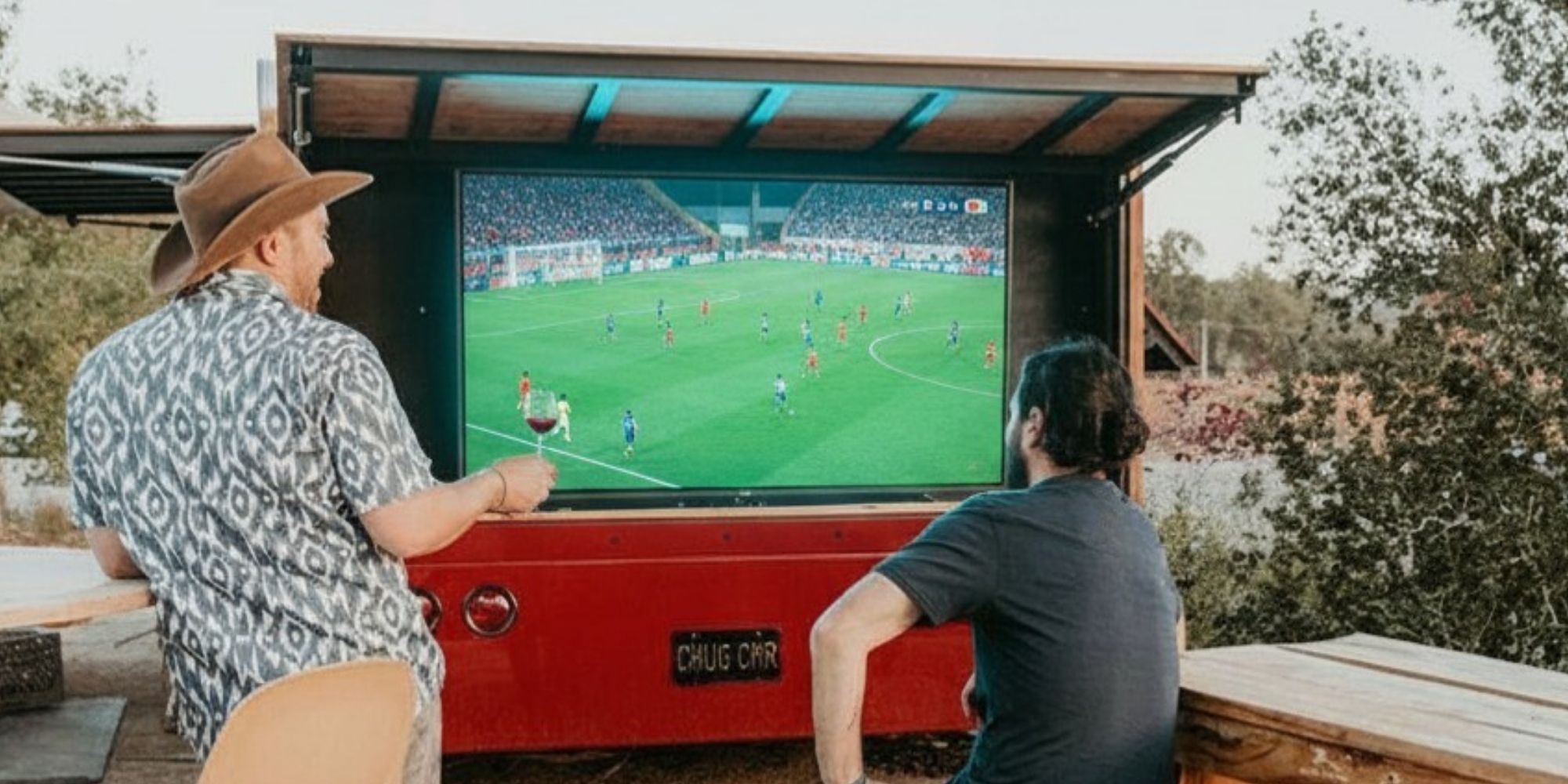 Two guys looking at a big screen at the Casino Mine Ranch Wine Truck watching the soccer matches.