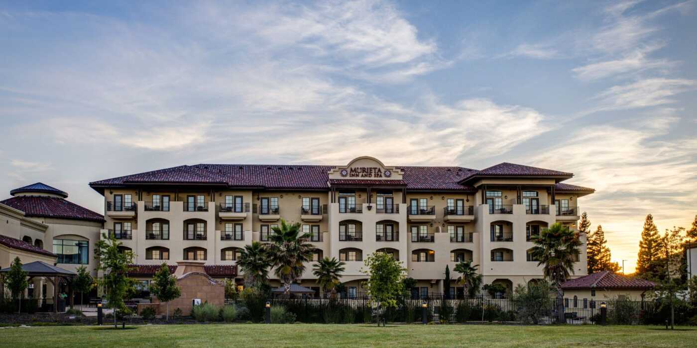 Murieta Inn & Spa's main hotel building with a blue sky and sun setting in the background.