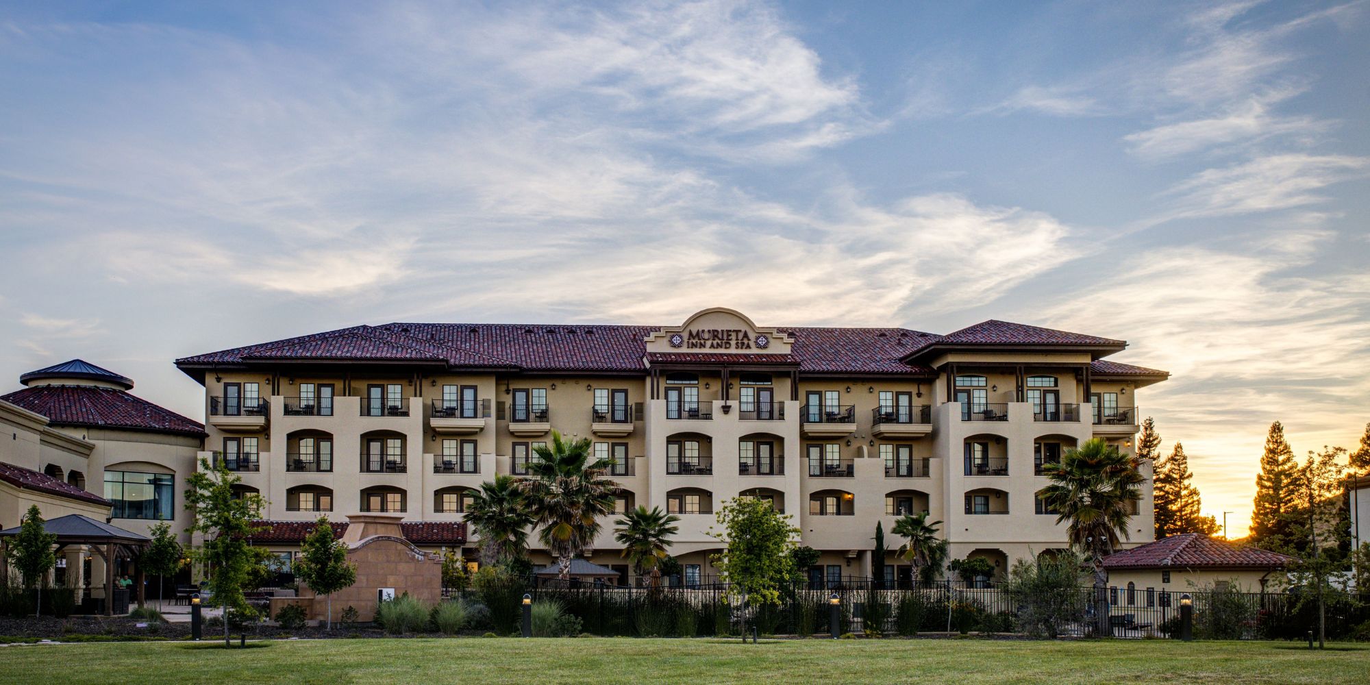 Murieta Inn & Spa's main hotel building with a blue sky and sun setting in the background.