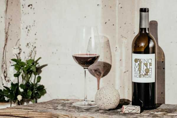 Casino Mine Ranch Mourvèdre opened wine bottle with a wine glass on a wooden tabletop.